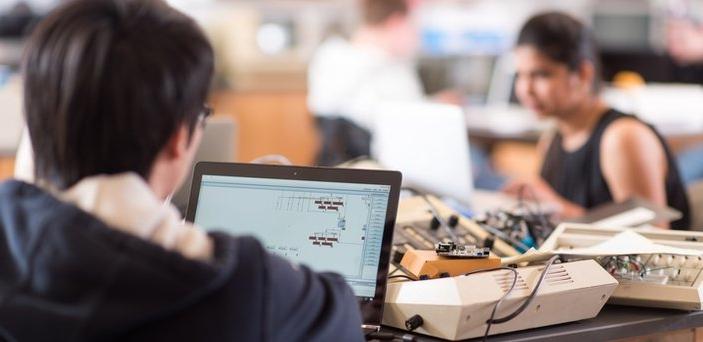 Students working on computers with electronic equipment on the table around them.